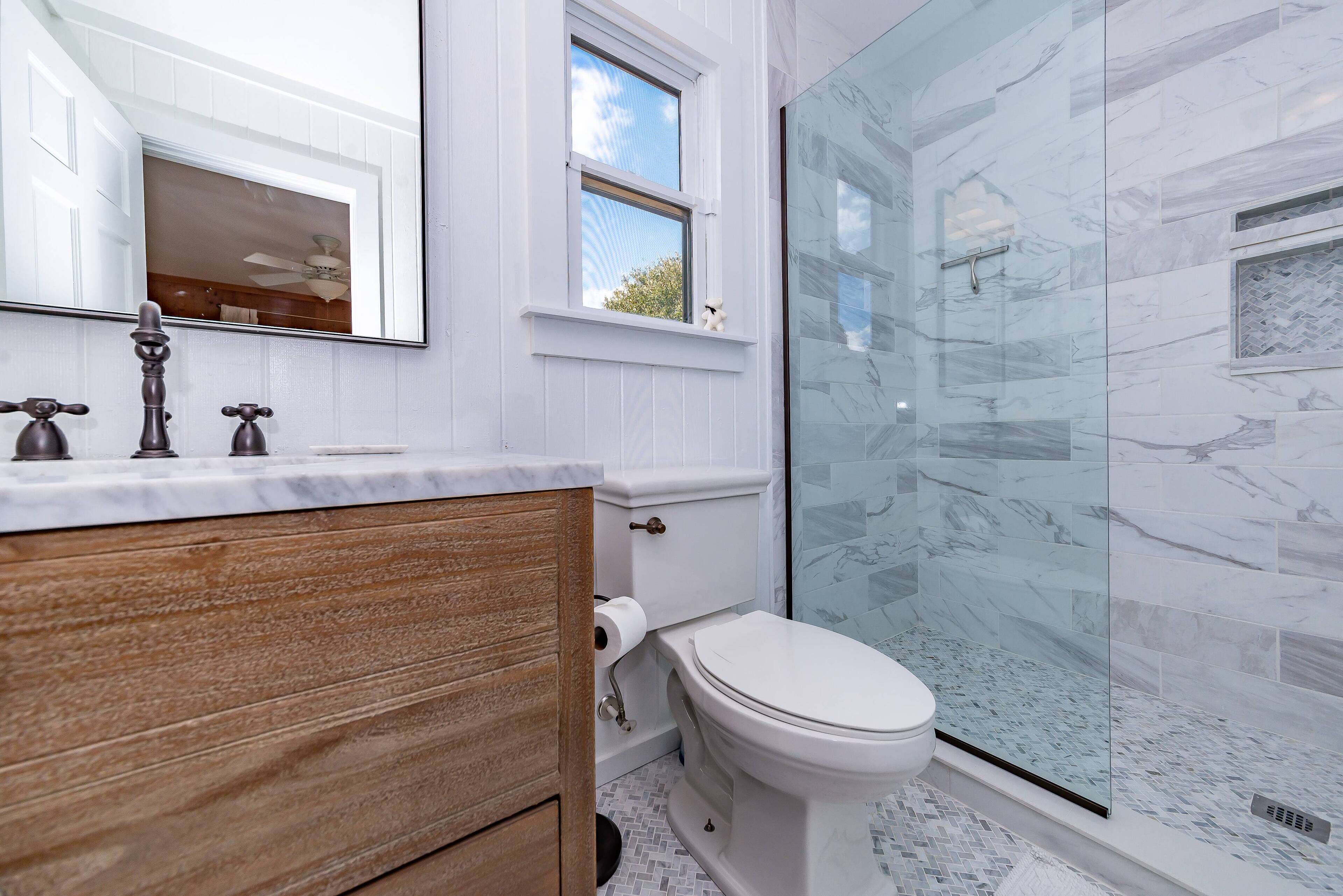 Een badkamer met een houten wastafelmeubel, een wit toilet en een douchecabine van glas.