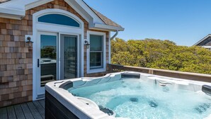 Ein Whirlpool auf einer Holzterrasse, im Hintergrund ein Haus.