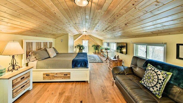 Een slaapkamer met een houten plafond, een bed, een nachtkastje, een dressoir, een bank en een raam.