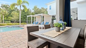 Zona junto a la piscina con mesa, sillas y una zona de estar cubierta.