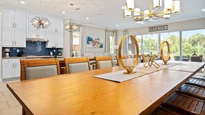Una cocina amplia con armarios blancos, una gran mesa de comedor de madera y un candelabro.