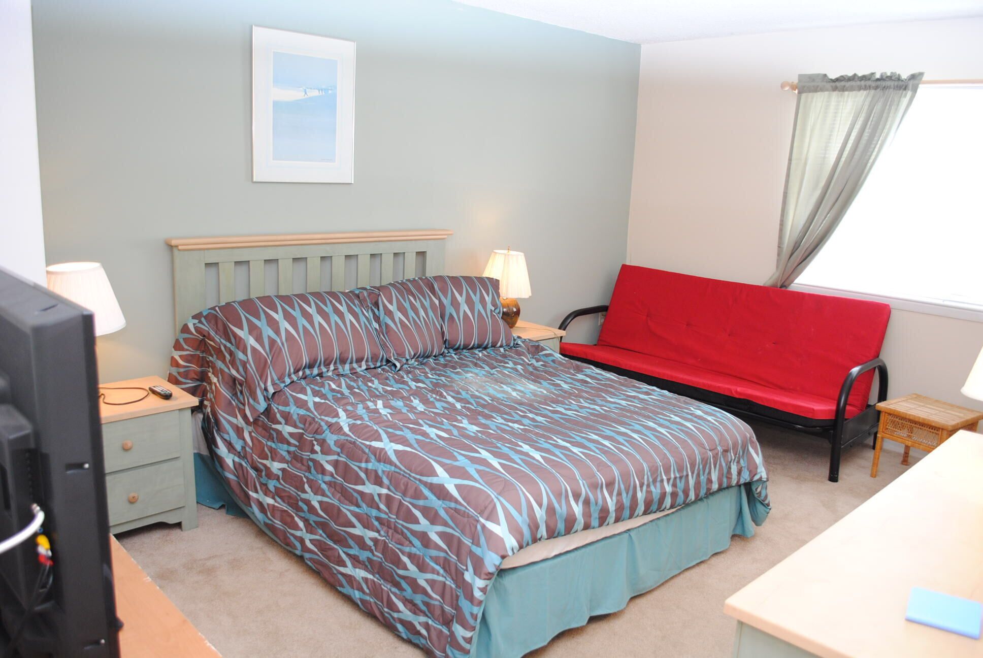 A hotel room with a bed, a red sofa, a desk, a lamp, and a picture on the wall.