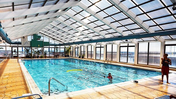 Une piscine intérieure dotée d’un plafond en verre transparent, d’un sol carrelé et offrant une vue sur l’extérieur.