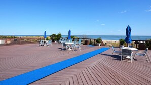 Une terrasse en bois avec des chaises et des parasols bleus, donnant sur la plage.