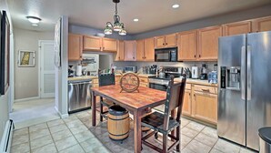 Una cocina con armarios de madera, electrodomésticos de acero inoxidable, una mesa de comedor de madera y un colgante de techo.