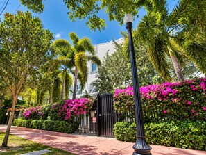 A pathway leading to a gated entrance with lush greenery and flowering plants. - South of Fifth 1BR Condo - Heated Pool, Balcony & Walk to Beach (Miami Beach)