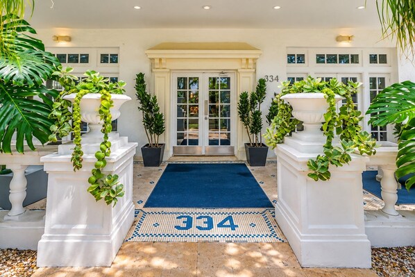 A hotel entrance with a number '334' on the floor, white columns with greenery, and a tiled floor leading to a glass door. - South of Fifth 1BR Condo - Heated Pool, Balcony & Walk to Beach (Miami Beach)