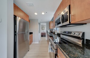 A modern kitchen with stainless steel appliances, wooden cabinets, and a granite countertop. - South of Fifth 1BR Condo - Heated Pool, Balcony & Walk to Beach (Miami Beach)