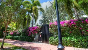 A pathway leading to a gated entrance with lush greenery and flowering plants.