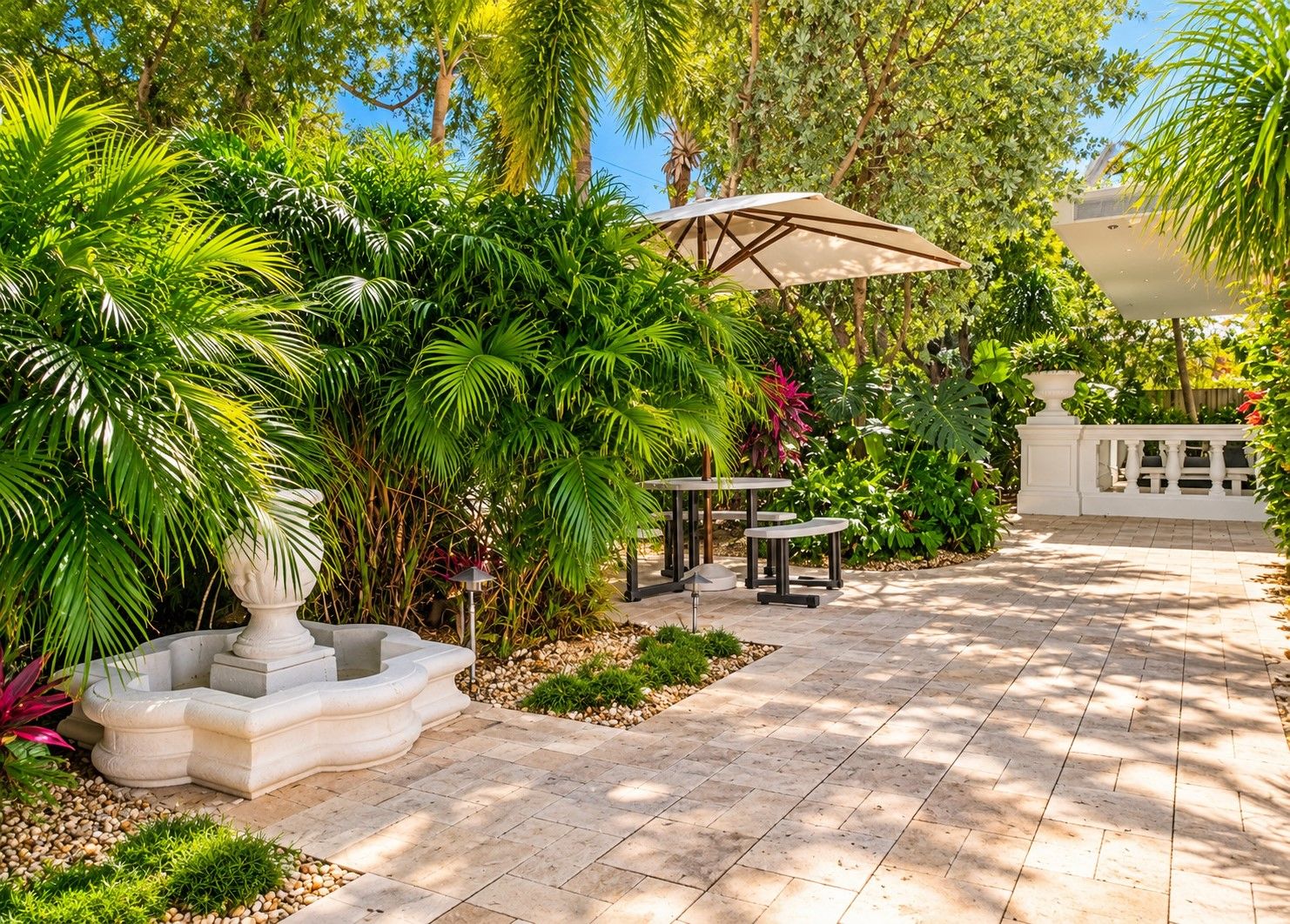 Un patio jardín con una fuente, mobiliario exterior y abundante vegetación.
