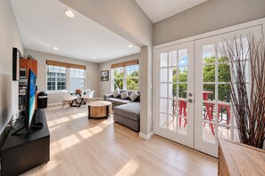 A modern living room with a flat-screen TV, a grey sofa, a round coffee table, and a dining area with a table and chairs. - South of Fifth 1BR Condo - Heated Pool, Balcony & Walk to Beach (Miami Beach)
