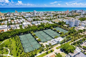 An aerial view of a coastal city with multiple tennis courts surrounded by residential buildings and palm trees. - South of Fifth 1BR Condo - Heated Pool, Balcony & Walk to Beach (Miami Beach)