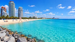 A beach with clear turquoise water, a sandy shore, and a row of modern high-rise buildings in the background. - South of Fifth 1BR Condo - Heated Pool, Balcony & Walk to Beach (Miami Beach)