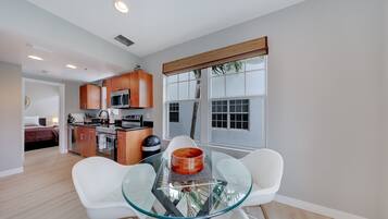 Una cocina moderna con armarios de madera, microondas y comedor con mesa de vidrio y sillas blancas.