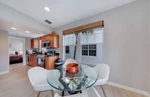 A modern kitchen with wooden cabinets, a microwave, and a dining area with a glass table and white chairs. - South of Fifth 1BR Condo - Heated Pool, Balcony & Walk to Beach (Miami Beach)