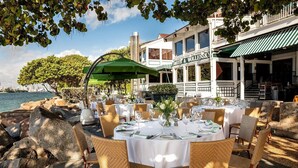 An outdoor dining area with tables set for two, overlooking a body of water, with a building labeled "SMITH & WOLENSKY" in the background.