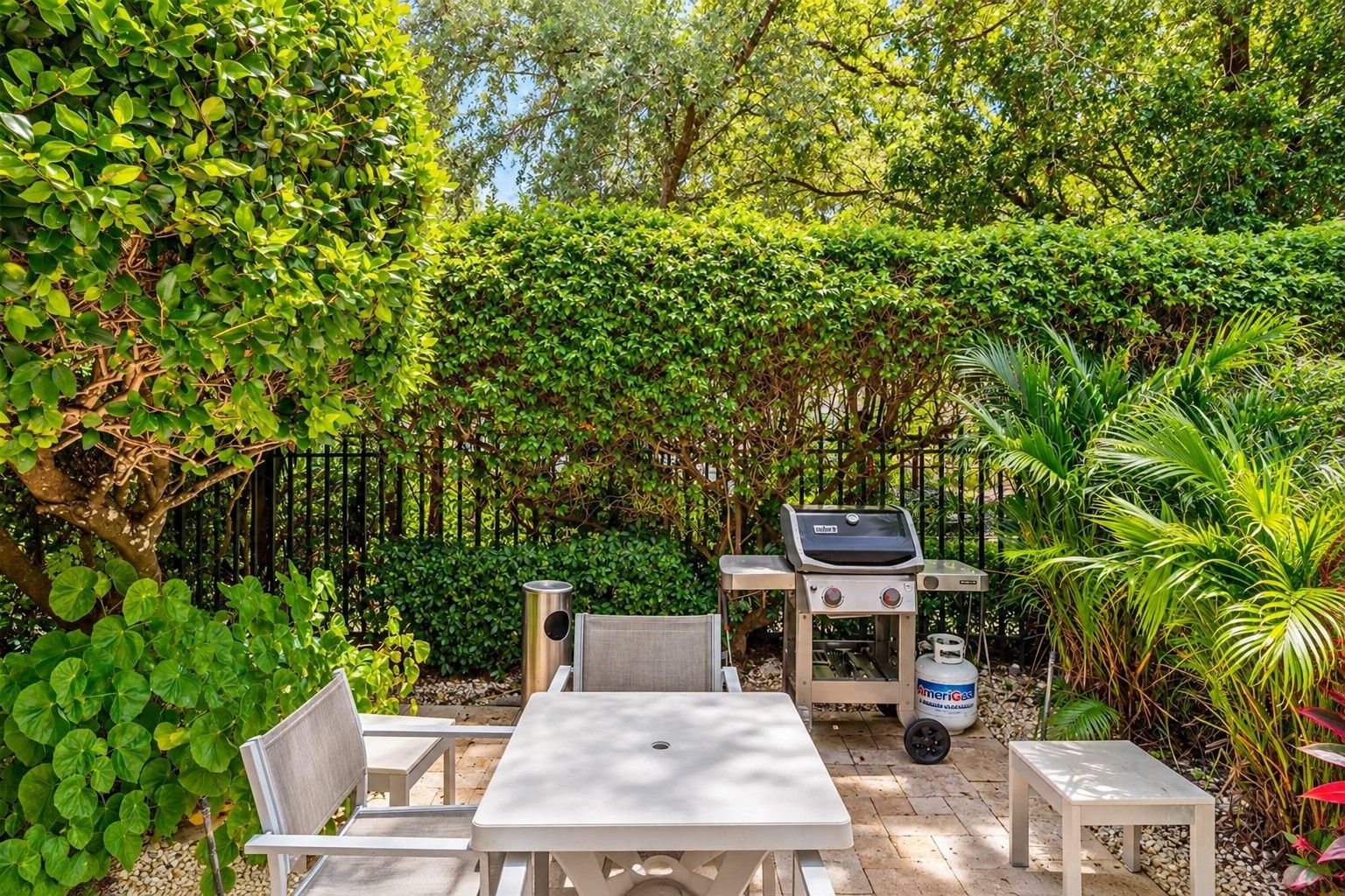Eine Terrasse mit Grill, Sitzgelegenheit und üppiger Bepflanzung.