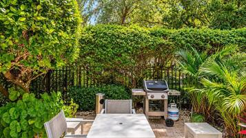 Eine Terrasse mit Grill, Sitzgelegenheit und üppiger Bepflanzung.