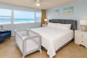 A hotel room with a bed, a crib, a nightstand, a lamp, and a view of the ocean.