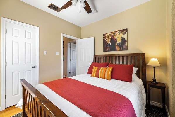 A hotel room with a bed, a painting, a lamp, and a ceiling fan.