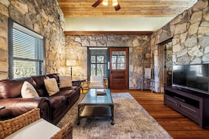 A stone-walled living room with a leather sofa, a coffee table, a TV stand, and a wooden ceiling.