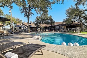 A swimming pool with lounge chairs, a stone building, and trees in the background. - 10 Bedroom Hill Country Retreat with Pickleball, Tennis and Pool- Stonehaven Ran (San Marcos)