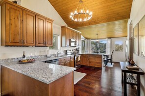 A kitchen with wooden cabinets, granite countertops, stainless steel appliances, and a wooden ceiling.