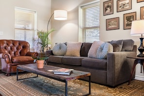 A living room with a leather armchair, a sofa, a coffee table, and a potted plant.