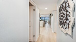 A hallway with a view to a kitchen and dining area, a decorative wall piece, and a door leading to another room.