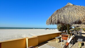 A beachside patio with a thatched umbrella, wooden lounge chairs, and a view of the beach.