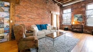 Un salon chaleureux avec un mur en briques, un canapé, un fauteuil à motifs, une table basse et un tapis.