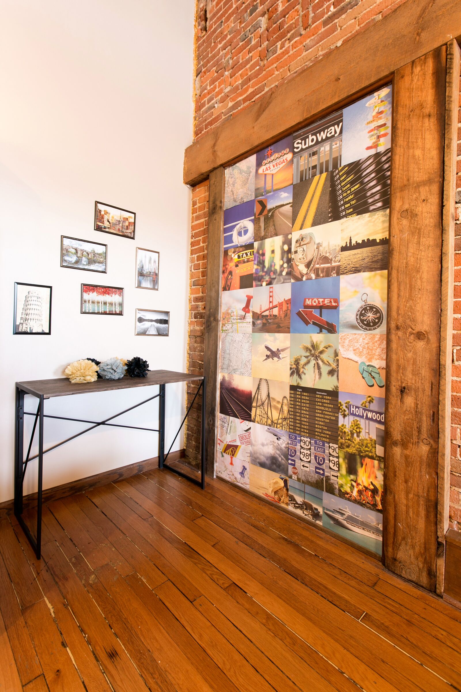A room with a wooden floor, a table with a cushion, and a wall with framed pictures and a collage of travel-related images.