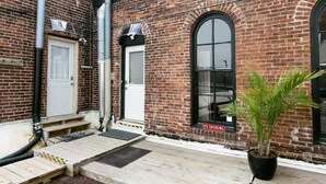 Un bâtiment en briques avec une porte blanche, une grande fenêtre en arc de cercle et un panneau indiquant « Défense de fumer ».