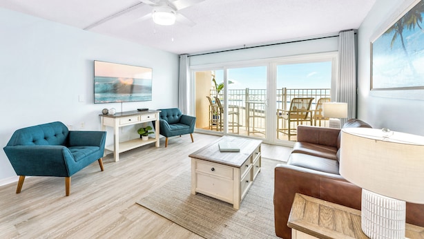 A modern living room with a sofa, armchair, coffee table, and a TV. There is a balcony with a view of the ocean. - Perfect for Families - Oceanfront Ground Floor Condo w/ Large Heated Pool! 🏖️ (Satellite Beach)