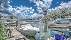 Un port de plaisance avec des bateaux amarrés, un phare en arrière-plan et un ciel dégagé.
