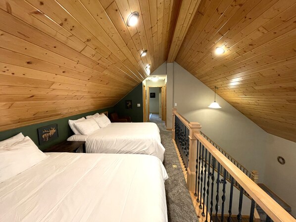 Una habitación con dos camas, vigas de madera en el techo, una escalera y un pasillo que conduce a otra habitación.