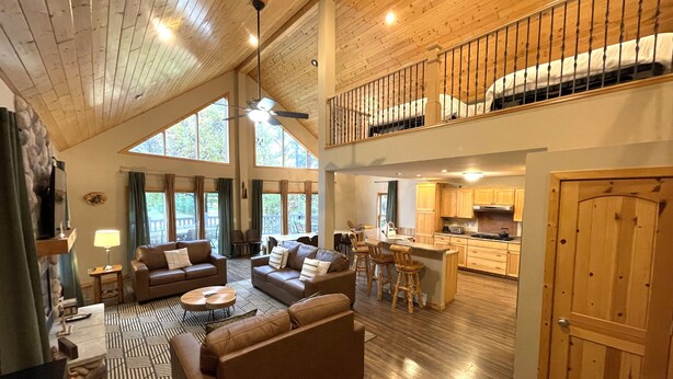 A spacious living area with a high ceiling, wooden floors, and a kitchen in the background.
