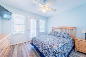 A bedroom with a bed, a wooden dresser, a nightstand, and a ceiling fan.