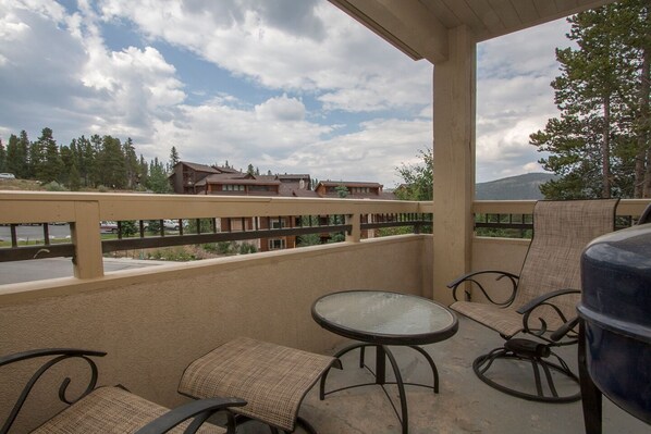 A covered outdoor patio with a table and chairs, overlooking a residential area with houses and trees.