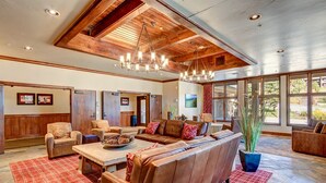 A spacious living room with a large sectional sofa, a coffee table, and a chandelier. There are wooden walls and a large window providing natural light. - Hot tub access, Ski-in/ski-out condo, Heated garage parking! (Breckenridge)
