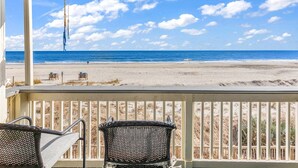 A beach view from a covered porch with two wicker chairs, a railing, and a distant view of the ocean and beach. - Completely Renovated Oceanfront Unit in Quaint Surfside Beach! SC205b (Surfside Beach)