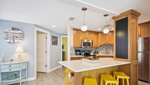 Une cuisine moderne avec des meubles en bois, un îlot central doté de tabourets, un four à micro-ondes et un réfrigérateur.