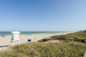 A beach with a lifeguard tower, beach umbrellas, and a grassy area in the foreground.