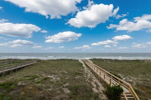 Une plage avec une promenade en bois qui mène à l’océan, sous un ciel partiellement nuageux.