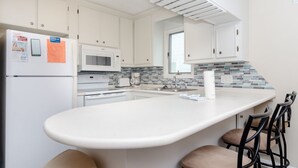 Een moderne keuken met witte kasten, een centraal kookeiland met barkrukken, een magnetron en een betegelde spatwand.