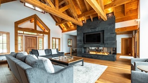 Un salón espacioso con chimenea de piedra, vigas de madera y grandes ventanales.