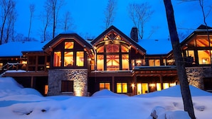 Un gran lodge de varios pisos con fachada de piedra y ventanas amplias, rodeado de nieve.