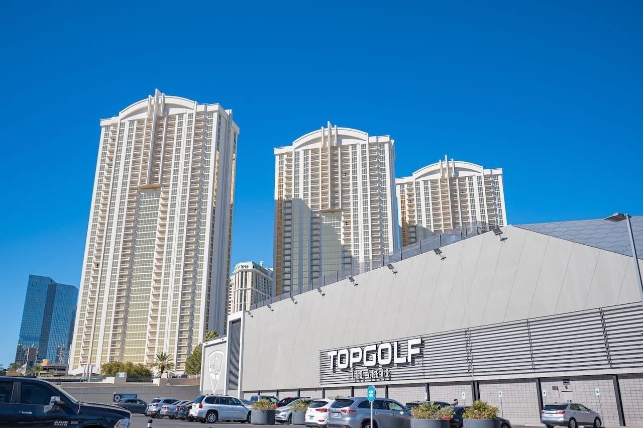 Un hôtel avec une grande enseigne sur laquelle on peut lire « TOPGOLF » et un parking où sont garées plusieurs voitures.