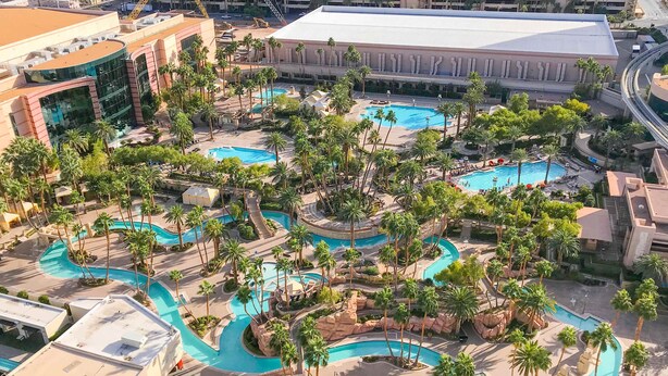 Vista aerea di un resort con diverse piscine, palme e un grande edificio sullo sfondo.