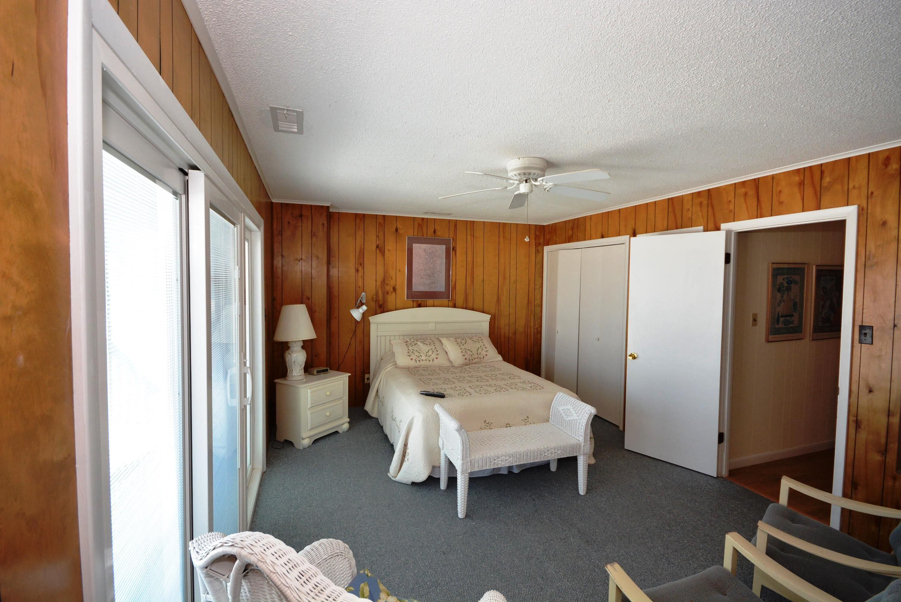 A bedroom with a bed, a ceiling fan, a nightstand, a lamp, a chair, and a wardrobe.